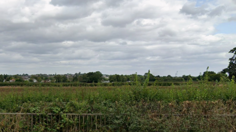 A field beyond a fence, with trees in the distance and grey clouds above