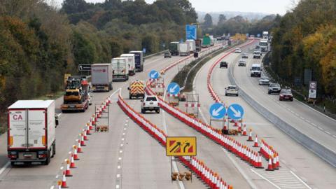 Hundreds of cones on a motorway. There are lorries queueing to the left and cars driving on the right.