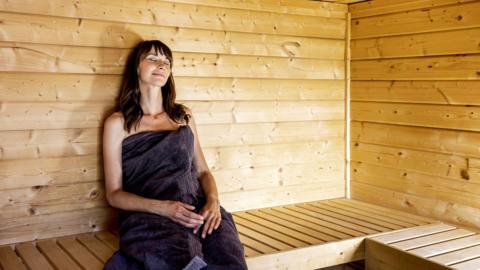 Woman wrapped in a grey towel relaxing in a sauna - stock photo