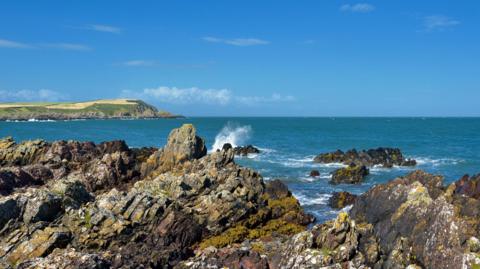 The rugged Solway coastline in southern Scotland with jagged rocks and a green piece of land jutting out into the water