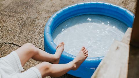 Child's feet in mid air over an inflatable paddling pool on a hot day.