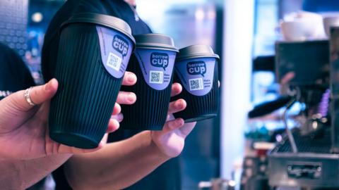 Three black reusable cups in a row with 'borrow a cup' written on them and a barcode.