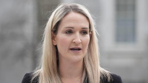 Helen McEntee, a woman with blonde hair. She is pictured from the shoulders up. The background of the image is blurred. 