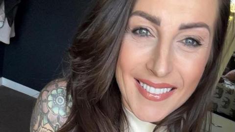 A close up of Kelly Bailey, who has long dark straight hair. You can see a colourful shoulder tattoo on her right arm.