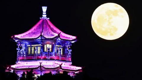  A bright yellow-tinged Moon beaming brightly over a pavilion in Guang'an in China's Sichuan Province lit up in purple lights.