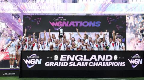 the England women's rugby team celebrating with the six nations trophy with purple flare guns going off behind them