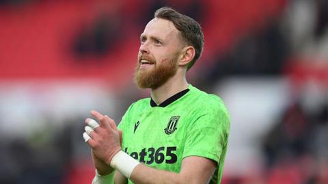 A smiling Viktor Johansson in a green short-sleeved Stoke goalkeeping jersey