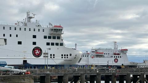 The front of the Manxman a tall boxy ferry, with three legs of man which reads Isle of Man Steam Packet Company, you can see the Ben-My-Chree in the background at Douglas Harbour.