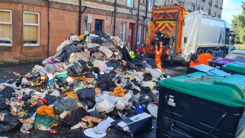 Waste spread across a residential street beside a refuse lorry.