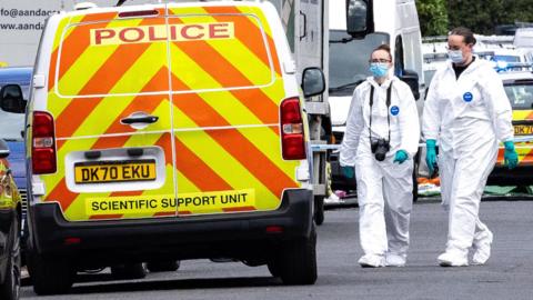 Police scientific support unit van and two female police officers in blue masks and white hazmat suits