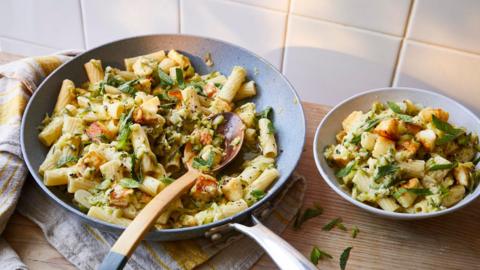 A frying pan and a plate, both full of pasta mixed with courgettes and halloumi