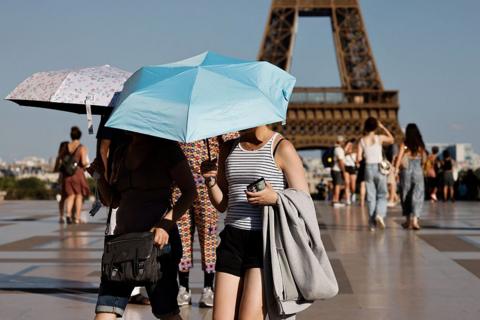 tourists walking near the eiffel tower holding up umbrellas to protect themselves from the sun