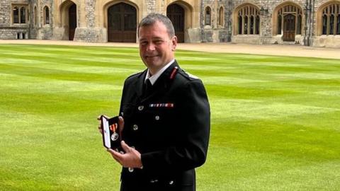 Gavin Tomlinson holding the King's Fire Service Medal in 2023 for distinguished service