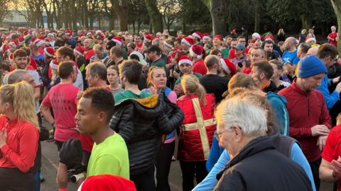 A very large group of people in running gear and festive outfits. One person is wearing a present costume.