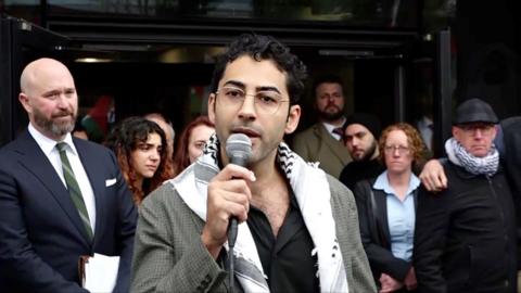 Mohsen Mahdawi speaks into a mic.
