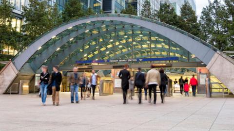 People are walking in and out of a modern entrance to an Underground station at Canary Wharf.