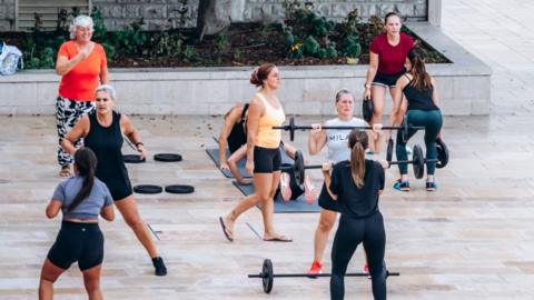 A group of women working out outside with mats and barbells.