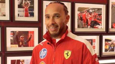 F1 driver Lewis Hamilton smiles. He is wearing a red Ferrari jacket