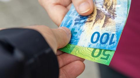 Two people handling Swiss Francs cash