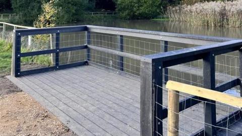 Grey wooden looking platform next to a pond