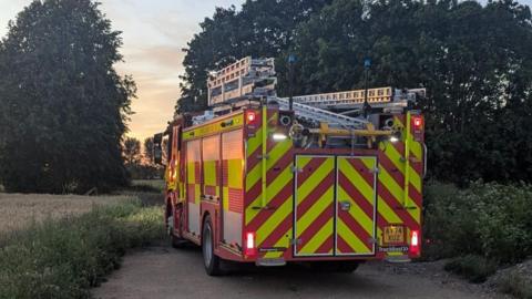 A red fire engine, parked up in between fields.