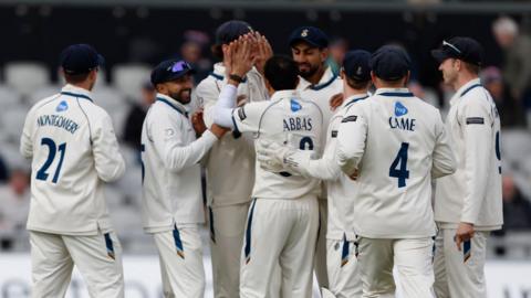 Mo Abbas with his back to the photo, is mobbed by Derbyshire team-mates