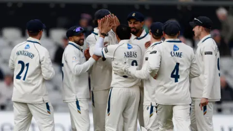 Mo Abbas with his back to the photo, is mobbed by Derbyshire team-mates 