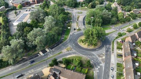 An aerial shot of a roundabout with four exits with trees alongside it, with the upgraded cycling and walking route visible on the left of the picture.