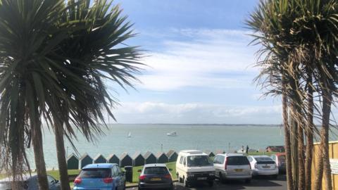 Gurnard Bay, Isle of Wight - beach huts are lined up along the sea front with a play area behind and the sea in front.