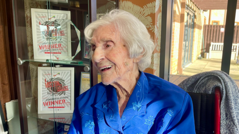 A woman with grey hair and a blue blouse laughing and sitting at her care home