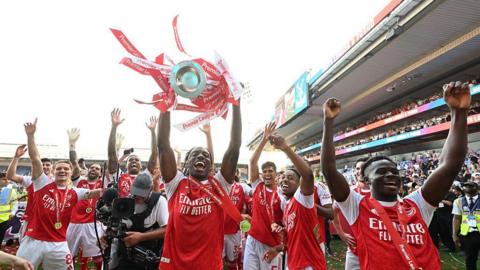 Noni Madueke lifts the Premier League trophy surrounded by his Arsenal team-mates