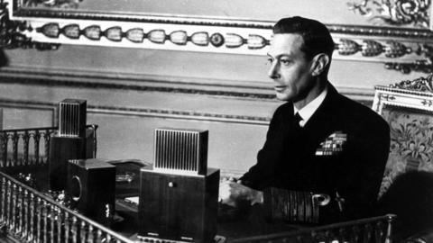 King George VI making a broadcast from a room in Buckingham Palace.