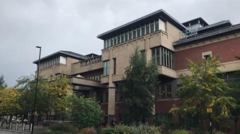 The front entrance to Sheffield Crown Court. Several trees and plants have been planted outside the building.