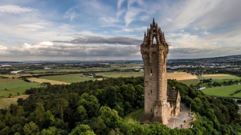 An aerial view of the Wallace Monument at Stirling and a view over trees and fields.