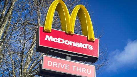 A large red McDonald's sign with the yellow arches with a blue sky in the background
