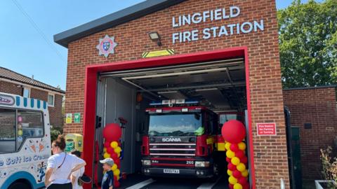The new Lingfield fire station. A fire engine can be seen in the new entrance, which has 'Lingfield Fire Station' at the top. There are balloons either side of the entrance and an ice cream van outside.
