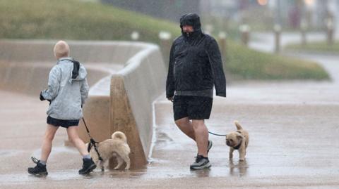 People walk their dogs in heavy rain in Blackpool