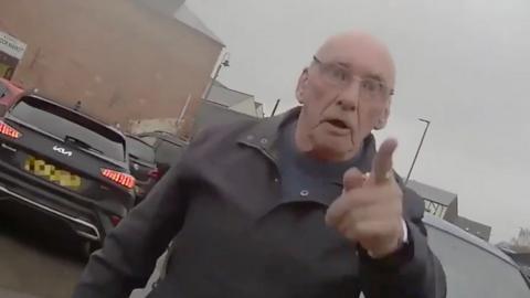  A man standing in a car park. He has his finger pointed at the person wearing the body-cam.