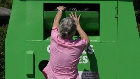 A woman putting recycling in a huge green skip