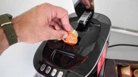 A man's hand is inserting a coffee pod into a coffee machine.