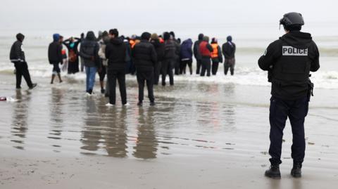 A police officer looks out to sea as a group of people wearing inflatable jackets stand in shallow water in Gravelines earlier this month.