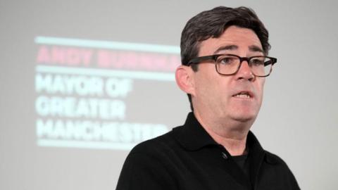 Andy Burnham stands in front of a screen with his name and title during a press conference