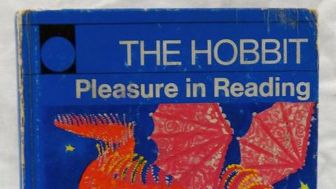 A book of The Hobbit by JRR Tolkien, under the publication series Pleasure in Reading, with an illustration on the front of a dragon.