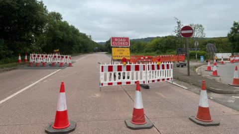 The picture shows an empty link road. There are three cones in the road and signs saying "Road closed".