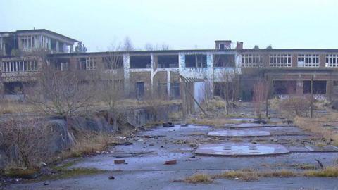 The deserted site of Huncoat power station. It is a long two-storey brick building with a taller section to the left which have been vandalised. To the front are overgrown flat areas with covers on the ground and sprouting weeds