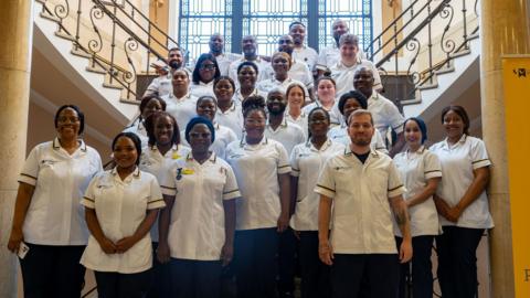 A group picture of nurses, wearing their uniform standing on a staircase and smiling at the camera