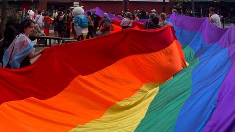 Pride attendees carry large rainbow flag through Oldham