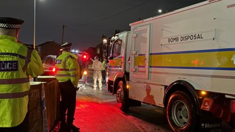 Police officers and Army personnel stand next to Bomb Disposal truck