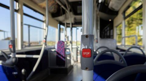 A close up of a stop button inside an empty bus with seats in mixture of fabrics and colours