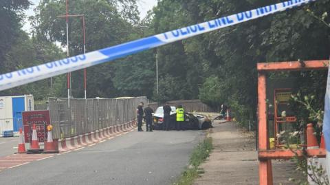 A group of police officers stand near two cars that have crashed. One side of the road is blocked off by roadworks.